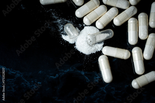 Open pill capsule and white powder in dark studio shot surrounded by pills . Concept with medicine and substance abuse and addiction. with negative space and .copy space