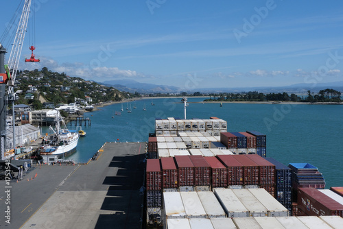 Container ship during cargo operation loading and discharging by mobile cranes operated by stevedores moored in port of Nelson, New Zealand.