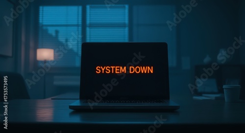 A laptop displaying a 'SYSTEM DOWN' alert in a dimly lit office environment, indicating a technical failure.