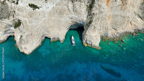 Aerial drone top down photo of inflatable rib boat anchored in paradise volcanic white cliff cove with crystal clear emerald sea and scenic caves