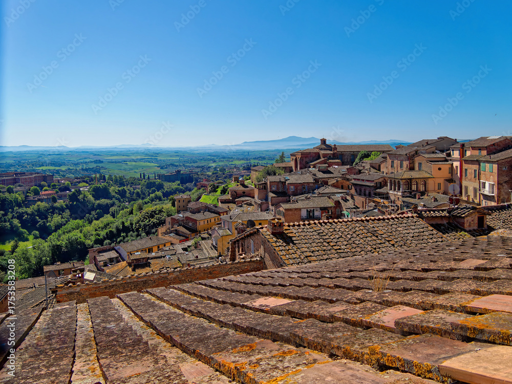 Obraz premium A sweeping Tuscan panorama where Siena’s terracotta rooftops meet verdant hills and a distant mountain under a radiant sky. Travel to Italy.