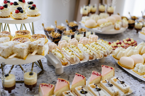 A beautiful assortment of delicate pastries, including cupcakes, macarons, and eclairs, elegantly displayed on a multi-tiered white stand for a wedding candy bar or festive celebration