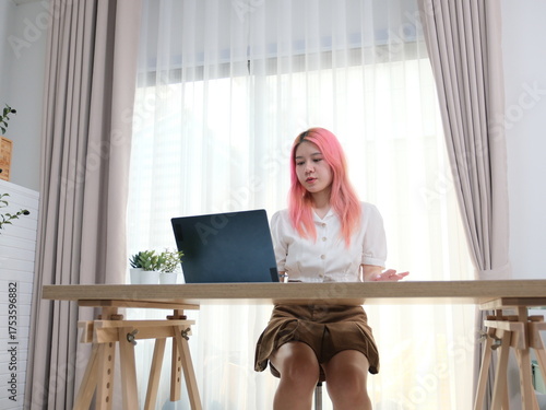 A woman with pink hair is sitting at a desk with a laptop