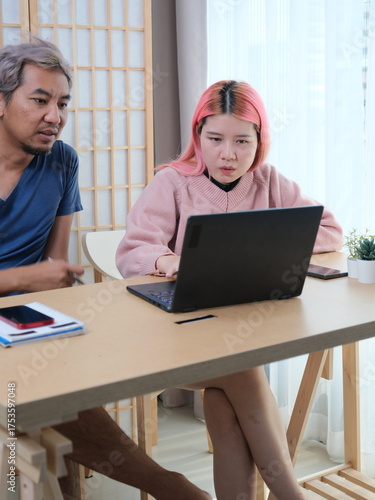 A woman with pink hair is typing on a laptop