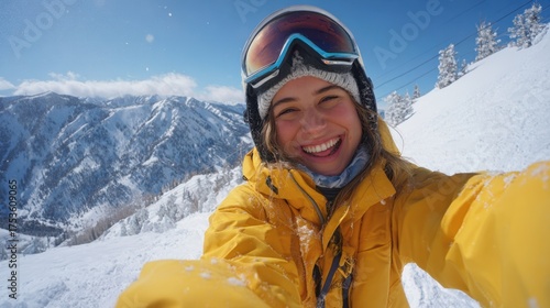 A skier smiles brightly while taking a selfie in a snowy mountain landscape. The sun shines on the peaks highlighting a joyful day of winter sports.