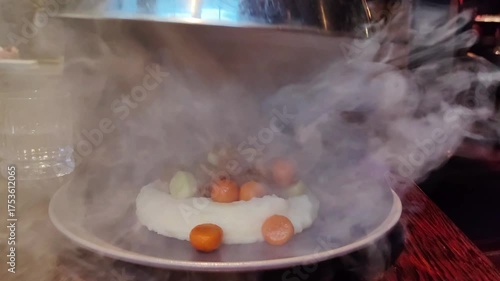 Waiter opens dish of mashed potatoes, boiled beef, and vegetables. Exquisite food presentation with steam effect in restaurant. Concept for food industry advertising and of modern cuisine.