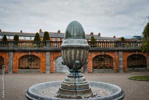 Quadro su tela Ornate stone fountain stands in front of a quaint brick building with arched windows and decorative balustrades