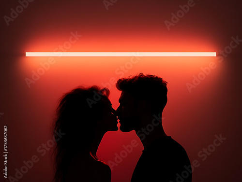Silhouetted couple sharing an intimate kiss under a glowing red light, conveying romance and connection in a minimalist setting.