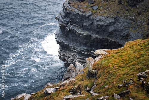 Εκτύπωση καμβά Dramatic sea cliffs overlooking the churning ocean, covered in lush green moss and weathered rock formations