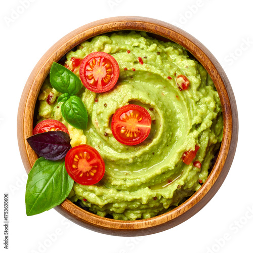 Overhead view of a rustic wooden bowl filled with vibrant, green mashed avocado with tomato and basil garnish