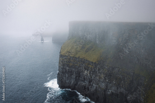 Photography Haunting misty cliffs overlooking the tumultuous sea, a lone figure stands silhouetted against the shroud of fog