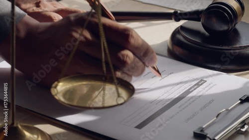 Close-up of hand signing legal contract with gavel and justice scales, symbolizing law and agreement.