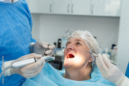  male dentist surgeon in uniform with assistant doing operation for install dental implant teeth of eldery woman