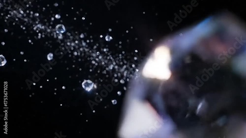 Sparkling water droplets spray against a luminous, faceted gem with a dark background.