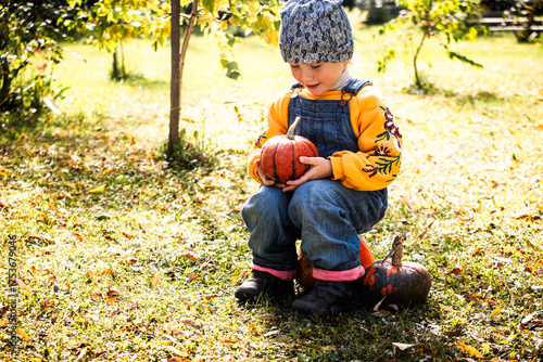 Little girl holding pumpkin outdoors in sunlight