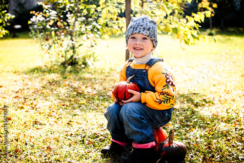 Smiling child sitting with pumpkin on autumn grass