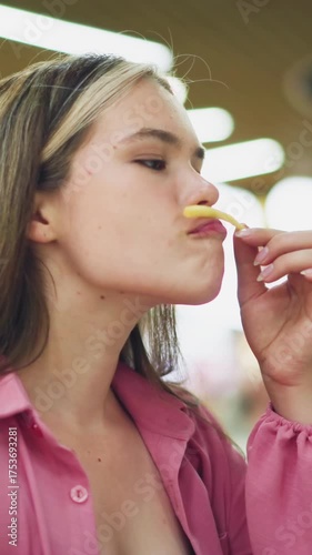 White lady in pink dress seated in restaurant playfully places potato chip on her upper lips, then removes it with a smile, with soft blur lights and vibrant colors from the restaurant