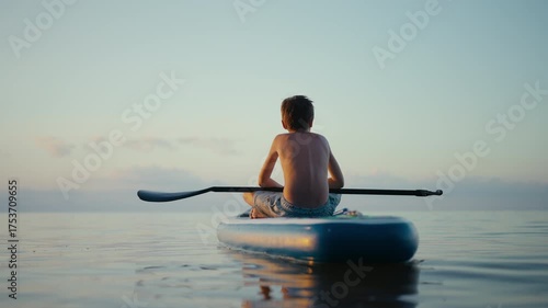 Wallpaper Mural Peaceful boy relaxing on paddleboard during golden hour sunlight Torontodigital.ca