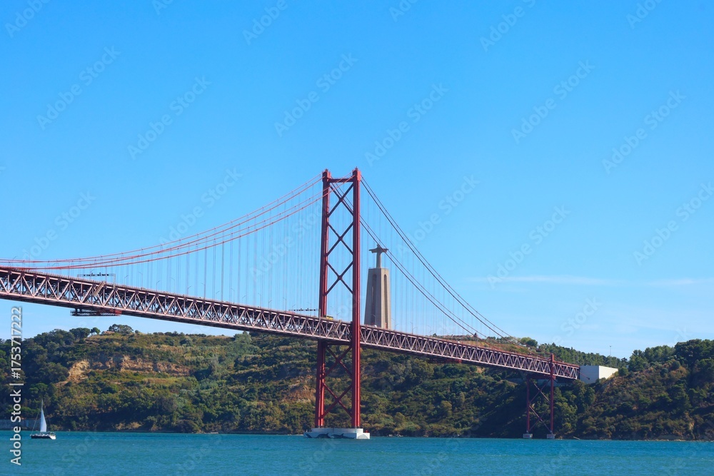 Fototapeta premium View of famous Lisbon bridge over Tagus river with Jesus Christ statue standing on the hill
