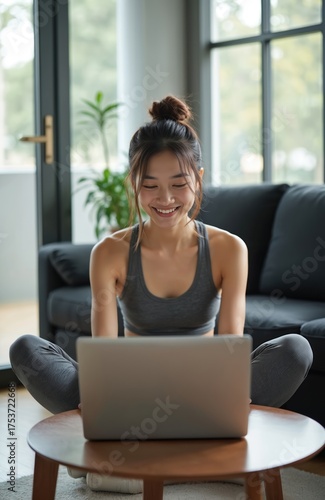 Smiling asian woman sits in sportswear on floor using laptop. She looks at screen. Concept of sport at home. Fitness coach records online workout session. Work from home. Free Download Smiling asian woman sits in sportswear on floor using laptop. She looks at screen. Concept of sport at home. Fitness coach records online workout session. Work from home. - GFXLoad
