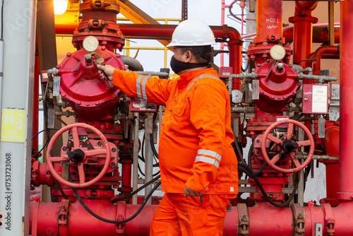 Technician in orange uniform inspects red fire suppression system valves for safety maintenance