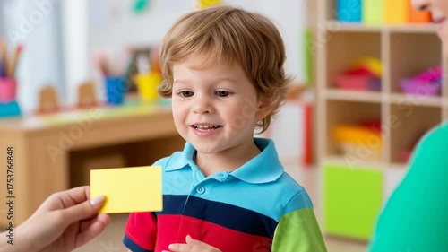 Caucasian toddler boy learning with flashcard in classroom. Teacher showing card during speech therapy or lesson. Early childhood education and development. Childcare, psychology, educational services