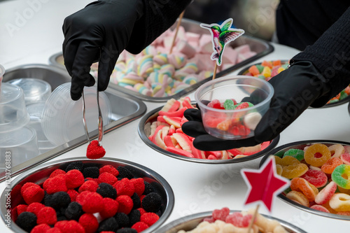 Snack bar cart with colorful and flavored candies and sweets, marshmallows, and fruit jellies for parties and events to serve in small cups.
