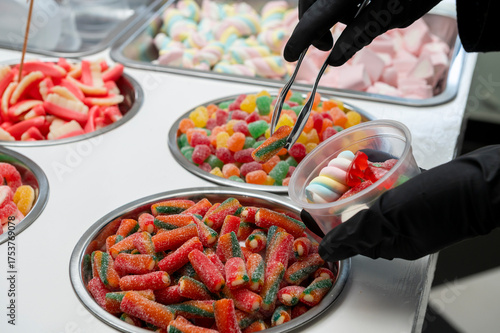 Snack bar cart with colorful and flavored candies and sweets, marshmallows, and fruit jellies for parties and events to serve in small cups.
