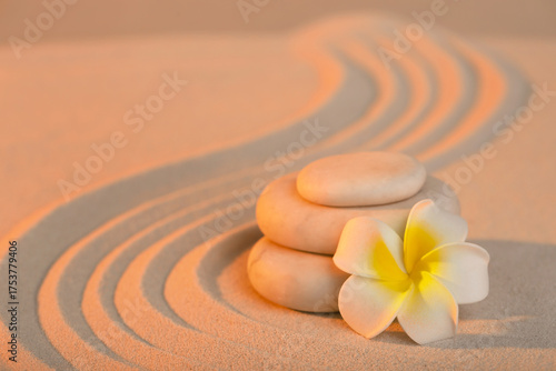 Photography Stack of spa stones with plumeria flower on light sand at sunset