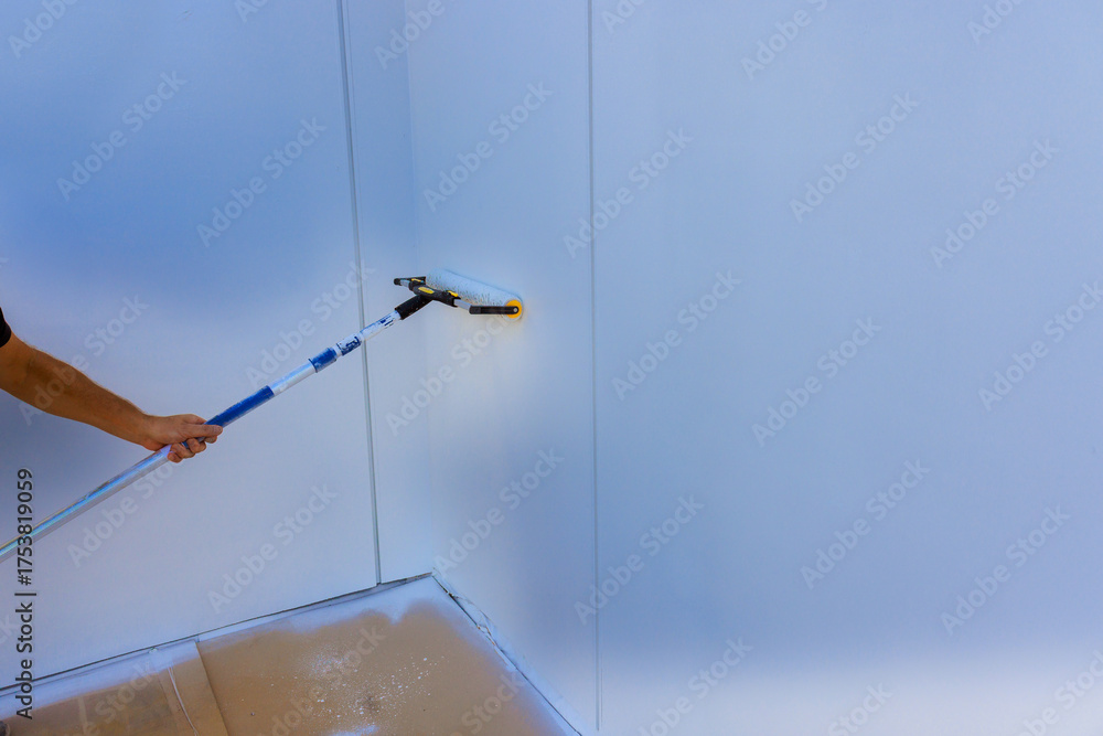 Obraz premium Handyman is using paint roller on wall in bright room, focusing on even coverage.