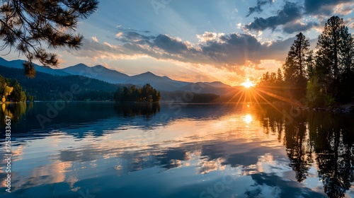 Fototapeta Naklejka Na Ścianę i Meble -  Sunburst over lake reflects mountains and trees at dawn.