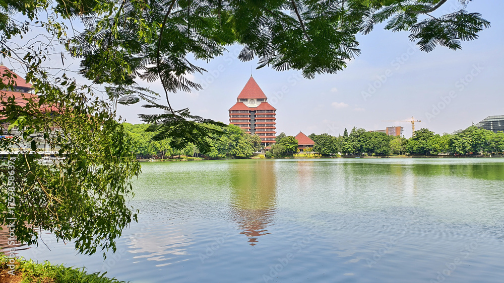 Obraz premium reflection of building on Kenanga Lake. Rectorate Building of the University of Indonesia. with trees as frame and blue sky