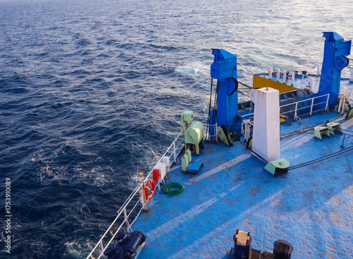 A boat's blue deck with a white railing overlooks the turbulent, foamy blue ocean water, showing the vessel's wake and some equipment. Makassar, Indonesia on June 16, 2025 