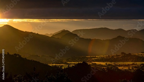 Serene sunrise over rolling hills, casting golden light on a misty valley with distant mountains