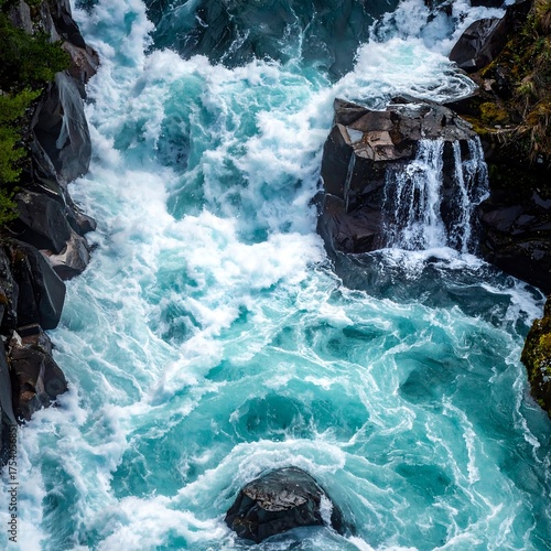 Aerial view of turquoise river rapids cascading over dark gray rocks with white foam