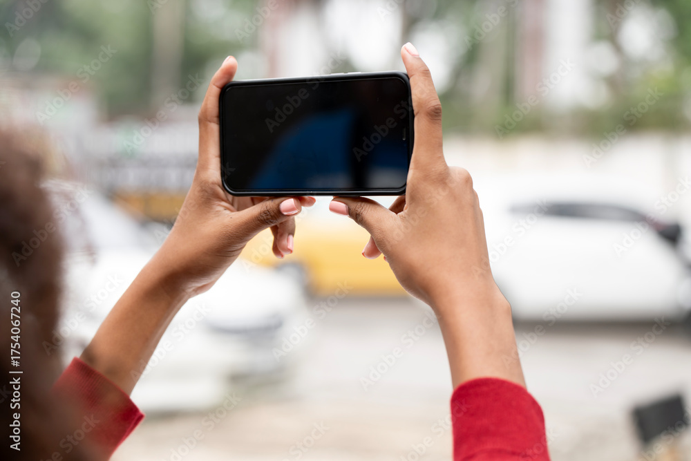 Fototapeta premium Hands holding a smartphone horizontally to capture a video or photo outdoors in an urban setting