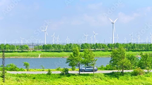 An electric car is driving outdoors, with a spinning windmill in the distance. Green new energy vehicle video