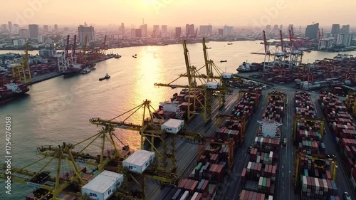 Aerial view of a busy port at sunset, with numerous gantry cranes, cargo ships, and stacked containers by a city skyline