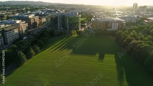 Aerial view of a sprawling green park amidst an urban landscape, bathed in golden hour light with long shadows