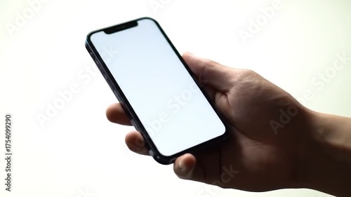Close-up of a hand holding a modern smartphone with a blank white screen against a bright background