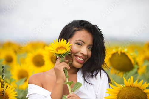 Obraz na płótnie A beautiful mulatto Latin woman with a white shirt brings it close to her face and flirts with a sunflower