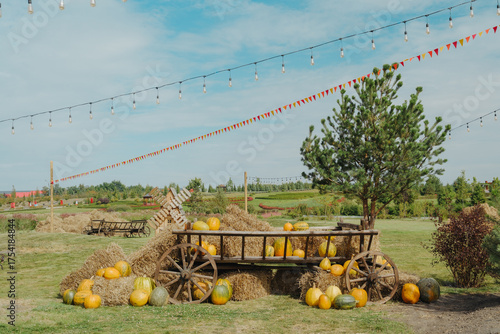 Harvest pumpkin display on rustic wooden cart surrounded by hay bales with outdoor lights