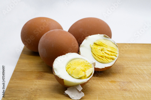  a boiled egg is cut in half, showing the texture of the white and yolk against the background of other whole eggs on the background of a wooden board