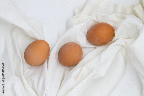 three whole eggs lie on a white cloth in a row along the folds