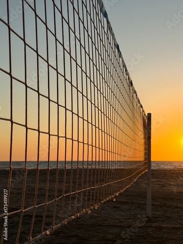 Sunset view through beach volleyball net with ocean and sand in background