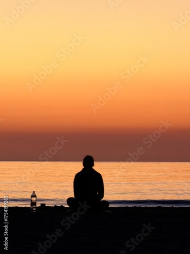 Person meditating on beach at sunset in peaceful solitude by the sea horizon. 