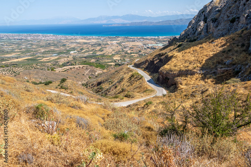 Scenic road leading to the ancient Acrocorinth hill overlooking the Corinthian plain and the blue sea in the distance