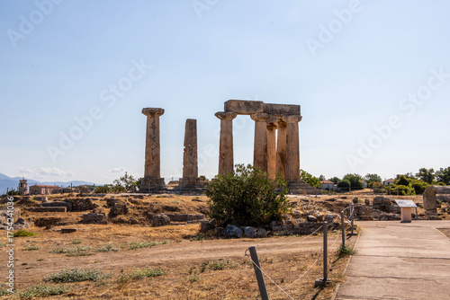 Ruins of the Temple of Apollo in Ancient Corinth, Greece. The surviving Doric columns stand against a clear blue sky, a symbol of classical Greek architecture.