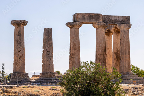 Ruins of the Temple of Apollo in Ancient Corinth, Greece. The surviving Doric columns stand against a clear blue sky, a symbol of classical Greek architecture.