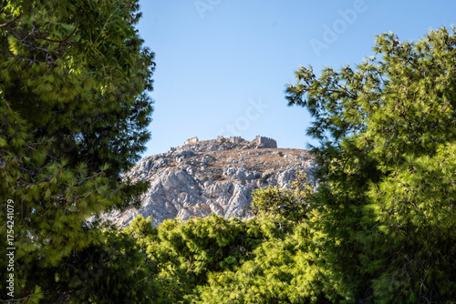 View of the medieval fortress on the slopes of Acrocorinth hill, surrounded by dry summer grass and blue sky. Historic landmark of the Peloponnese.